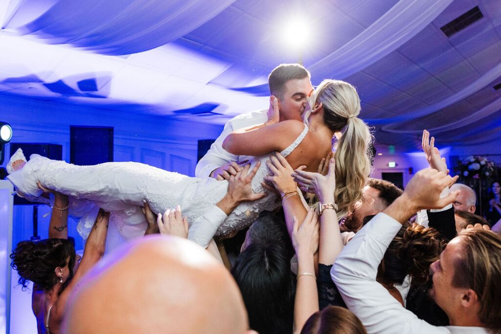 Bride and groom kiss and crowdsurf at Flowerfield wedding reception.
